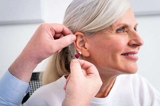 Ältere Frau bekommt ein modernes Hörgerät eingesetzt, Hörgeräte Anpassung Beratung.